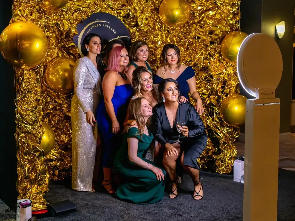 Guests posing in front of a gold sequin wall beside the ring-light photo booth at a New York gala