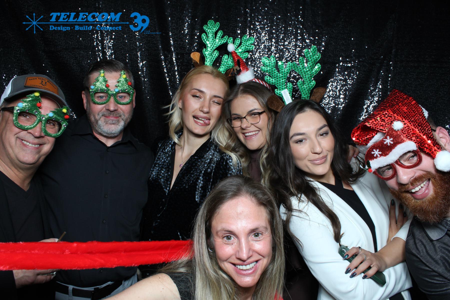 TELECOM team posing with a red feather boa and Christmas props at the 39th anniversary party